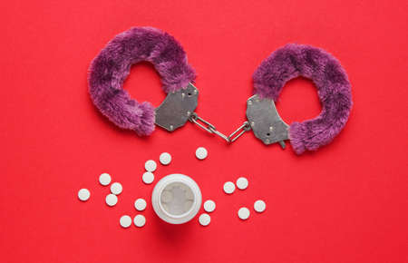 Sex stimulation. Handcuffs for sex games with pills on red background. Sexual bdsm toy. Fetish, erotic concept. Top viewの写真素材
