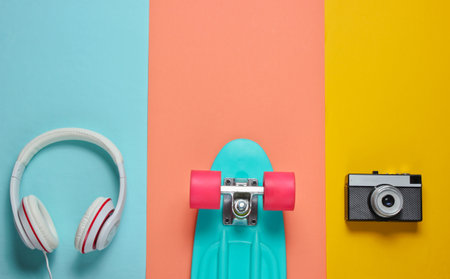 Hipster outfit. Skateboard with headphones, retro camera on colored background. Creative fashion...