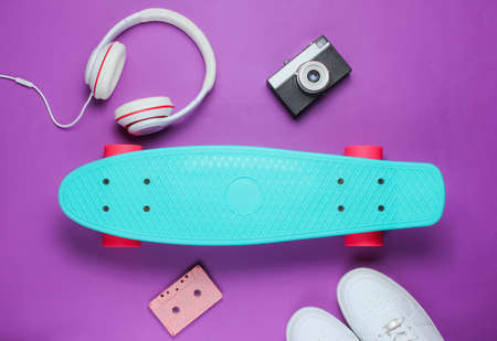 Hipster outfit. Skateboard with headphones, sneakers, retro camera, audio cassette on purple background. Creative fashion minimalism. Trendy old fashionable style. Minimal summer fun. Music concept. Top viewの写真素材