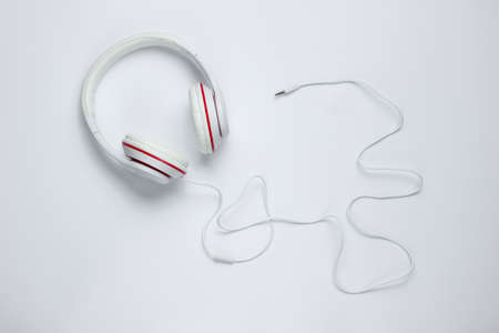 Classic white wired headphones with cable on white paper background. Retro style. 80s. Pop culture. Top view. Minimal Music Conceptの写真素材