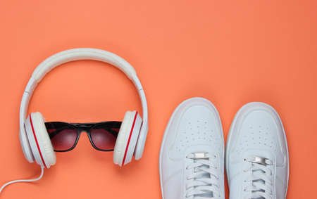 White Sneakers and headphones with sunglasses on coral color background. Casual design. Music concept. Flat lay, minimal.の写真素材