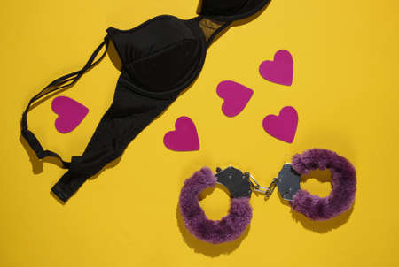 Handcuffs for sex games, hearts and black bra on yellow background. Sexual bdsm toy. Fetish, erotic concept. Top viewの写真素材