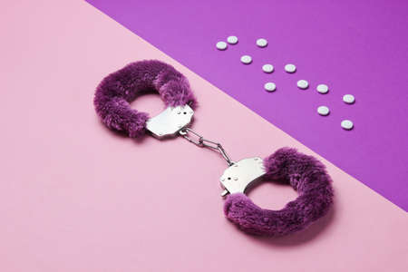 Sex stimulation. Handcuffs for sex games with pills on purple pink background. Sexual bdsm toy. Fetish, erotic concept. Top viewの写真素材