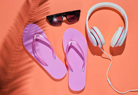 Accessories for relaxing on the beach. Flip flops, headphones, sunglasses. Studio shot on pink background with palm leaf shadow. Top viewの写真素材