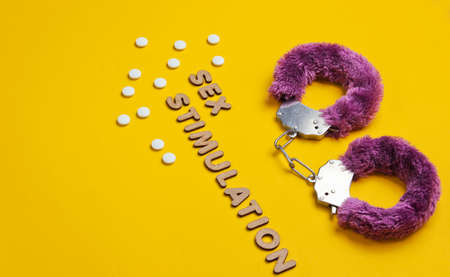 Sex stimulation. Handcuffs for sex games with pills on yellow background. Sexual bdsm toy. Fetish, erotic concept. Top viewの写真素材