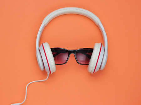 Modern headphones with sunglasses on coral color background, flat lay. Creative music concept. Retro style.の写真素材