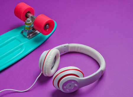 Hipster outfit. Skateboard with headphones on purple background. Creative fashion minimalism. Trendy old fashionable style. Minimal summer fun. Music conceptの写真素材