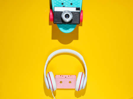 Hipster outfit. Skateboard with headphones, audio cassette on yellow background. Creative fashion minimalism. Trendy retro 80s style. Minimal summer fun. Music concept. Top viewの写真素材