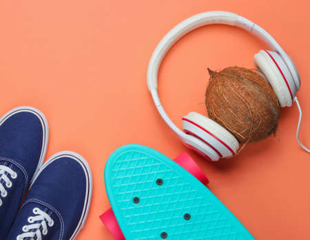 Hipster fashion look. Skateboard, sneakers, coconut with headphones on coral background. Top view. Flat layの写真素材