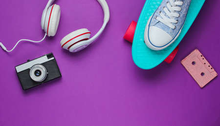 Hipster outfit. Skateboard, headphones, audio cassette, sneakers, retro camera on purple background. Creative fashion minimalism. Minimal summer fun. Pop art. 80s. Copy space. Top viewの写真素材