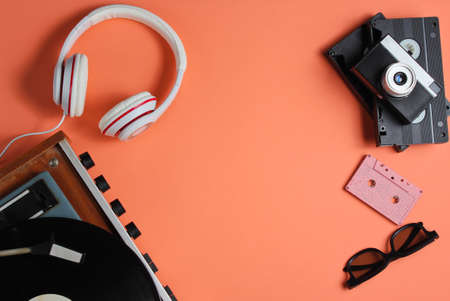 Flat lay retro 80s pop culture objects. Vinyl player, headphones, audio cassette, video tapes, film camera on coral color background. Copy space. Top viewの写真素材