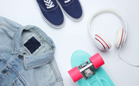 Hipster fashion look. Denim jacket, skate, sneakers, headphones on a white background. Top view....