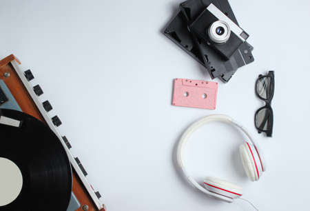 Flat lay retro 80s pop culture objects. Vinyl player, headphones, audio cassette, video tapes, film camera on white background. Copy space. Top viewの写真素材
