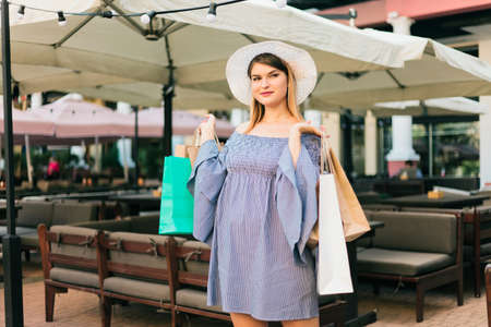 Happy shopping concept. Young attractive woman in a hat and dress holds shopping bags in her hands and smiles in a summer cityの写真素材