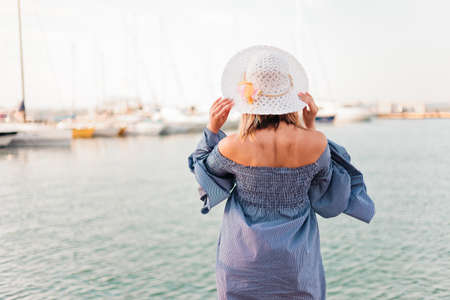 Young attractive woman in a fashionable hat and stylish dress on a background of the sea. Back view