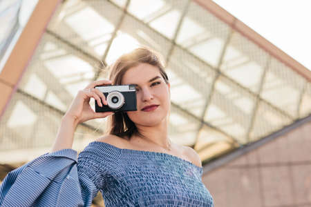Portrait of a young blonde woman photographer in a dress with a retro camera outdoorsの写真素材