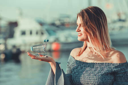 Shopping concept. Mini shopping trolley stands on the palm of a woman's hand outdoorの写真素材