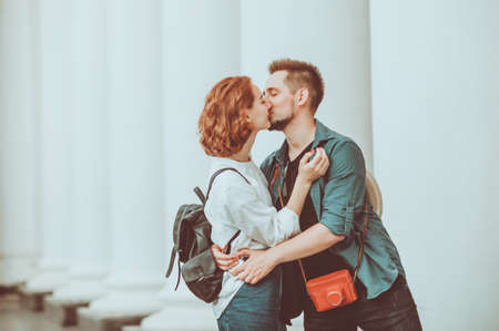 Romantic portrait of a young couple of hipsters in love kiss against white columnsの写真素材