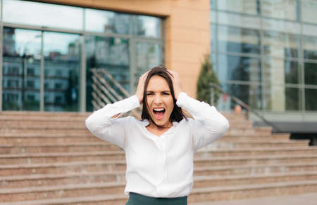 Young hysterical business woman screaming and holding her head her arms against the background of a business centerの写真素材