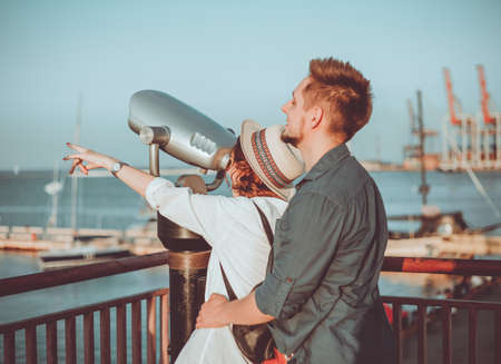 Young couple in love looks through city binoculars at the sea station. Romantic walk in an unfamiliar cityの写真素材