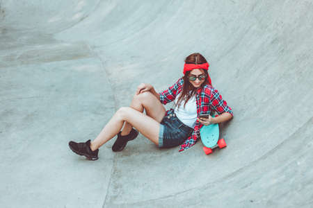 Youth pastime. Young hipster woman resting with a skateboard at a skateparkの写真素材