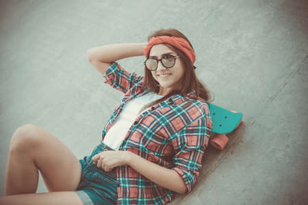 Youth pastime. Young hipster woman resting with a skateboard at a skateparkの写真素材