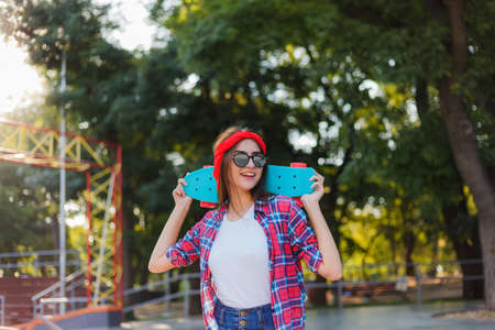 Youth sport. Young attractive hipster woman wearing a red plaid shirt and denim shorts holding a skateboard in a skatepark. Summertimeの写真素材