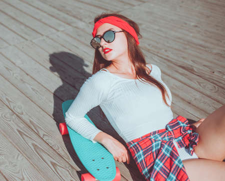 Portrait of stylish skater woman at beach. Attractive sexy woman lies on skate outdoorの写真素材