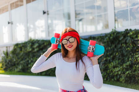 Portrait of stylish dressed young woman with skateboard outdoors on bright sunny dayの写真素材