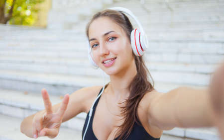 Selfie portrait of a cheerful sport woman in headphones. Healthy lifestyle. Gesture Vの写真素材
