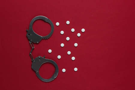 The concept of corruption in medicine. Pills and handcuffs on red background. Medical still life....