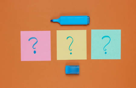 Memo pieces of paper with drawn question marks, felt-tip pen on brown background. Top viewの写真素材