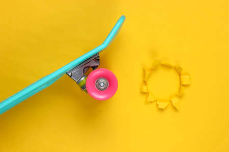 Plastic mini cruiser board on yellow background with torn hole. Pastel color trend. Summer fun. Youth minimalistic concept. Top viewの写真素材