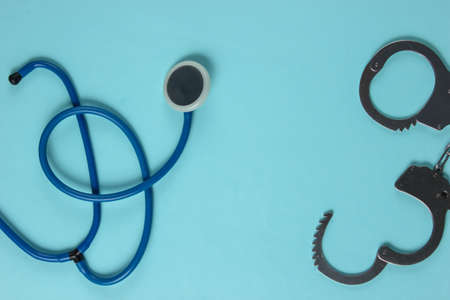 Medical crime. Stethoscope and steel handcuffs on a blue background. Top view