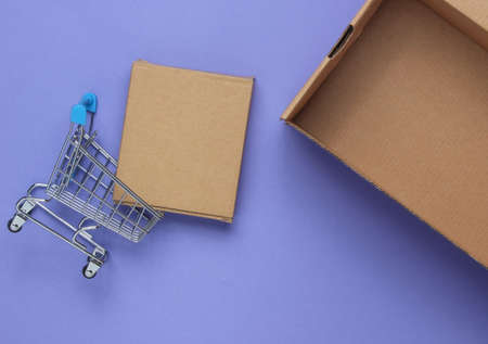 Gift delivery concept. Cardboard boxes and mini shopping trolley on purple background. Top view.