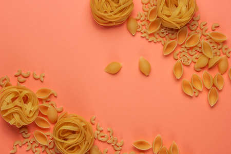 Different types of raw italian pasta on coral color background. Top view.