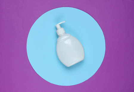 White shampoo bottle on a purple background with a blue pastel circle in the middle. Top view. Minimalistic beauty concept.の写真素材