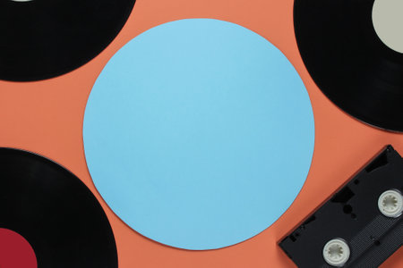 Retro vinyl records, video cassette on coral color background with a blue circle for copy space. Top...