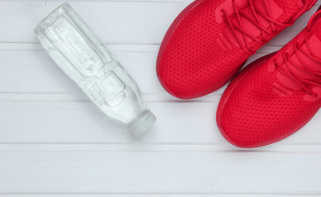 Red sports shoes for running, bottle water on white wooden floor. Top view.