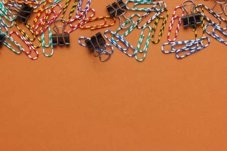 Lot of colored paper clips on brown background. Minimalistic office concept. Copy spaceの写真素材