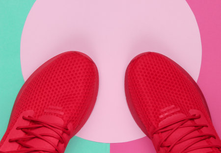 Red sport sneakers on colored background with pink pastel circle. Youth hipster concept. Top view