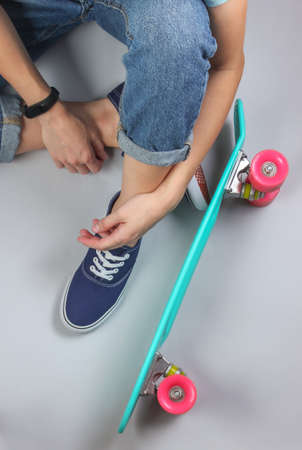 Youth hipster concept. Female legs in jeans and sneakers sitting on white background with cruiser...