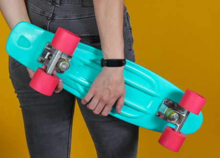 Young slim woman in jeans holds plastic cruiser board in her hands on yellow background. Youth...