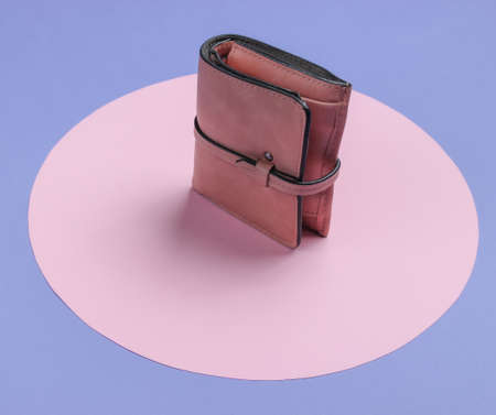 Stylish women's leather wallet on a purple background with a pink pastel circle. Creative...