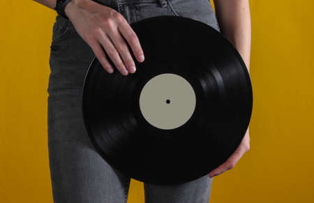 Woman in jeans with vinyl record on yellow background. Crop photoの写真素材