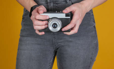 Woman in jeans holds a retro film camera on a yellow background. Crop photoの写真素材
