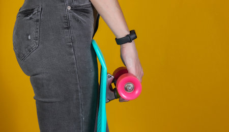 Young slim woman in jeans holds plastic cruiser board in her hands on yellow background. Youth...