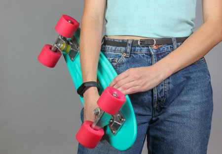 Young slim woman in jeans holds plastic skate board in her hands on a gray background. Youth hipster...