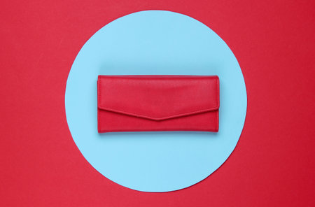 Stylish women's red leather wallet on red background with blue pastel circle. Creative minimalistic fashion still life. Top viewの写真素材