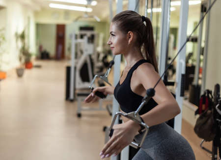 Young attractive fit woman doing exercise in crossover exercise machine at gym
